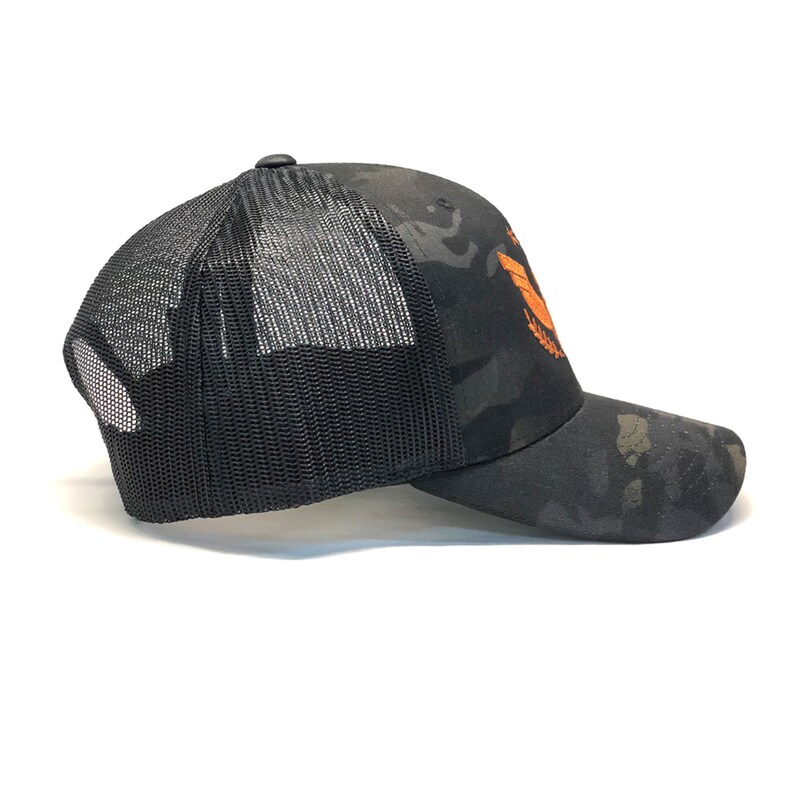 Puede incluir: Gorra de camionero de camuflaje negro con parte trasera de malla negra y visera curva. La gorra presenta un emblema naranja en la parte delantera. Adecuada para uso informal y actividades al aire libre.