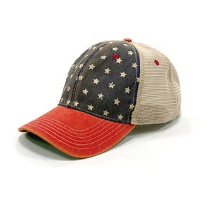 May include: A red, white, and blue baseball cap with a mesh back. The front of the cap is made of a distressed denim fabric with white stars printed on it. The bill of the cap is red.