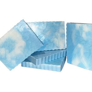 Op de afbeelding: Een stapel van vier blauwe en witte gemarmerde zeepstaven. De zeepstaven hebben een golvende rand en zijn in een stapel gerangschikt.