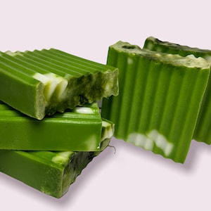 Op de afbeelding: Een stapel van vier groene en witte gestreepte zeepstaven. De zeepstaven zijn gemaakt met natuurlijke ingrediënten en hebben een frisse, schone geur.