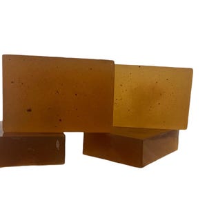 May include: Four bars of amber-colored soap stacked on top of each other. The soap has a speckled appearance.