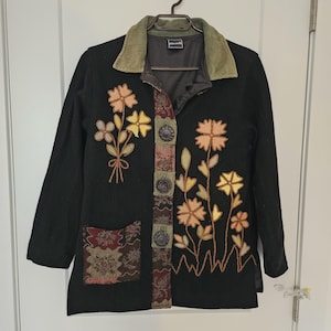 May include: Black jacket with floral embroidery in orange, yellow, and green. It has a corduroy collar and decorative fabric panels with button closures. Includes a pocket with a patterned design.