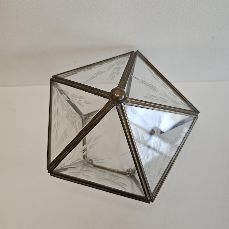 May include: A clear glass box with a brass frame. The box is shaped like a pyramid and has etched designs on the glass.