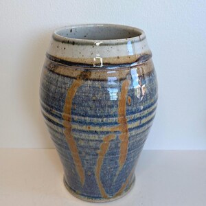 May include: A ceramic vase with a wide, rounded body and a tapered neck. The surface features a speckled cream-coloured rim, transitioning into a deep blue glaze with vertical, amber-toned drip patterns and horizontal bands around the centre.