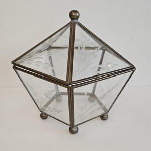 May include: A clear glass box with an etched floral design, framed in brass with a brass knob on the lid. The box sits on four small brass feet.
