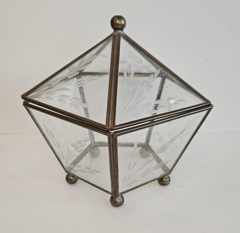 May include: A clear glass box with an etched floral design, framed in brass with a brass knob on the lid. The box sits on four small brass feet.