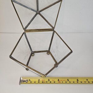 May include: A clear glass geometric box with a brass frame and etched details. The box is open and has a hinged lid. The box is approximately 25 cm wide.
