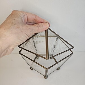 May include: A clear glass box with a brass frame and etched floral design. The box has a hinged lid and sits on four small brass feet.