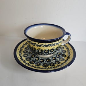 May include: A yellow and blue teacup and saucer set with a swirling pattern. The cup and saucer are made of ceramic and have a traditional design.