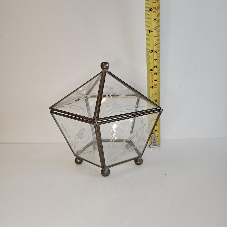 May include: A clear glass box with an etched floral design and a brass frame. The box has a hinged lid and sits on four small brass feet.