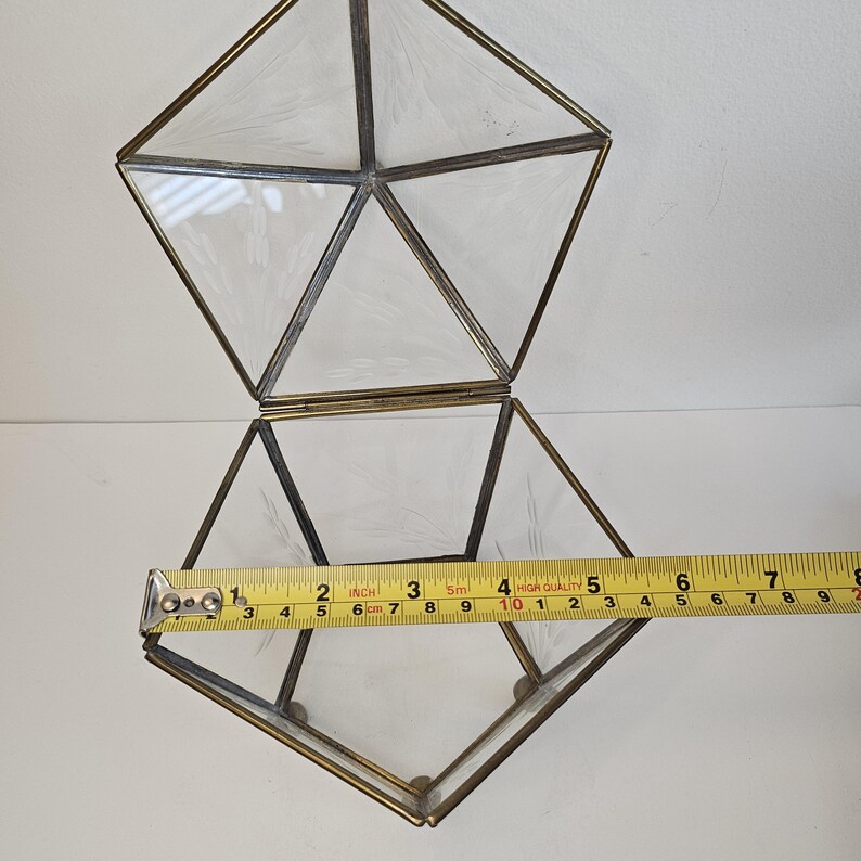 May include: A clear glass geometric box with a gold metal frame. The box is open and the lid is resting on top. The box is 15 cm wide.