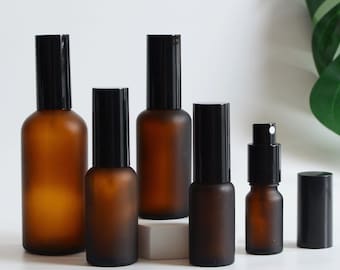 May include: Set of six amber glass bottles with black spray tops. The bottles are various sizes and are arranged in a row on a white surface.