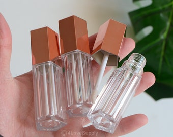 May include: Four clear lip gloss tubes with rose gold lids. The tubes have a hexagonal shape and are made of clear plastic. The lids are shiny and have a metallic finish.