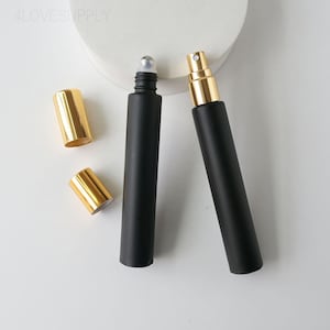 May include: Black perfume bottles with gold-colored caps and spray nozzle. One bottle has a rollerball applicator, the other a spray nozzle. The caps are cylindrical. The bottles are on a white surface.
