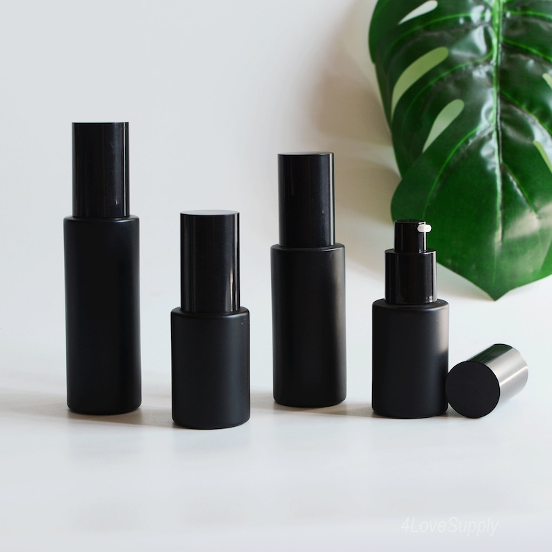 Puede incluir: Cuatro botellas de vidrio negro esmerilado con diferentes tapas de bomba y tapones. Las botellas est&aacute;n dispuestas en una fila sobre una superficie blanca.