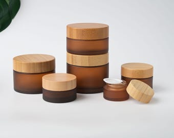 May include: A collection of amber-colored glass jars with bamboo lids. The jars are in various sizes, some stacked, and one has its lid off. The jars are arranged on a white surface. The text "LOVESUPPLY" is visible in the top left corner.