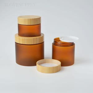 May include: Four amber glass jars with bamboo lids and a separate bamboo ring. The jars are cylindrical, with a frosted finish. One jar has a white lid. The text "4LOVESUPPLY" is visible in the top left corner.