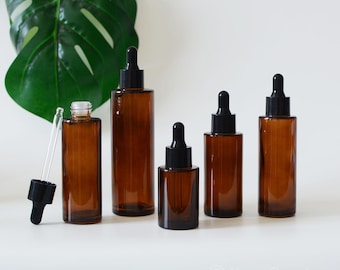 May include: Five amber glass bottles with black dropper tops. The bottles are arranged in a row from largest to smallest. The bottles are on a white surface.