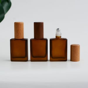 May include: Three amber glass roll-on bottles with wooden caps. One bottle has a silver rollerball top. The bottles are square and have a frosted appearance. The wooden caps are cylindrical and vary in colour.