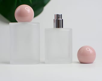Könnte beinhalten: Zwei parfümflaschen aus mattiertem Glas mit rosa kugelförmigen Kappen. Eine Flasche ist zylindrisch, die andere rechteckig mit einem silbernen Zerstäuber. Der Text "4LOVESUPPLY" ist oben links sichtbar.