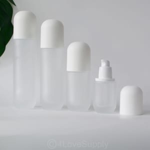 Peut inclure: Ensemble de cinq flacons en verre givré avec des bouchons blancs. Les flacons sont de tailles différentes et ont une forme ronde.