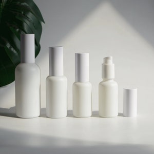 May include: Five white frosted glass bottles with different sized caps and pump tops. The bottles are arranged in a row from largest to smallest on a white surface.