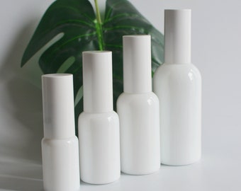 May include: Four white glass bottles with white caps, arranged in a row from smallest to largest. The bottles are empty and have a smooth, rounded shape.