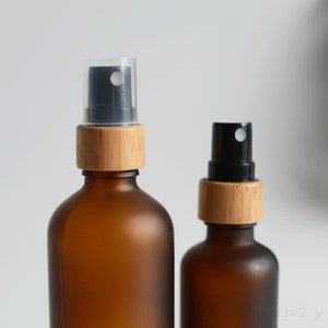 May include: Two amber glass bottles with black spray tops and bamboo lids. The bottles are frosted and have a matte finish.