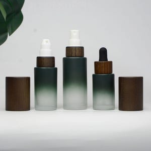 May include: Three glass bottles with wooden caps and spray or dropper applicators. The bottles have a gradient effect, transitioning from dark green to frosted white. Two wooden caps are separate from the bottles.