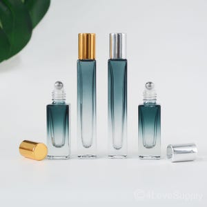 May include: Set of three glass roller bottles with a gradient blue color. The bottles have gold and silver caps and are perfect for essential oils or perfumes.