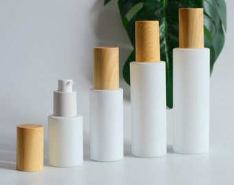 May include: Four white frosted glass bottles with wooden caps. The bottles are different sizes and are arranged in a row from largest to smallest.