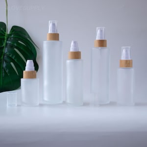 Puede incluir: Cinco botellas de spray de vidrio esmerilado con cuellos de bambú y tapas transparentes están dispuestas sobre una superficie blanca. Las botellas varían en tamaño, con la botella más grande en el centro. La palabra "LOVESUPPLY" está en la esquina superior izquierda.