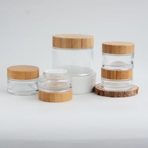 Peut inclure: Plusieurs pots en verre transparent avec des couvercles en bambou. Les pots sont de différentes tailles et formes, certains empilés. Les couvercles sont en bambou brun clair. Certains pots sont sur un bloc blanc ou une tranche de bois.