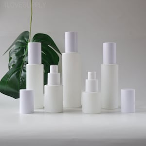 Puede incluir: Una colección de botellas cosméticas blancas y pulverizadores con tapas blancas. Las botellas varían en tamaño y forma, algunas con un diseño cilíndrico y otras con una estructura escalonada. El fondo incluye una gran hoja verde.