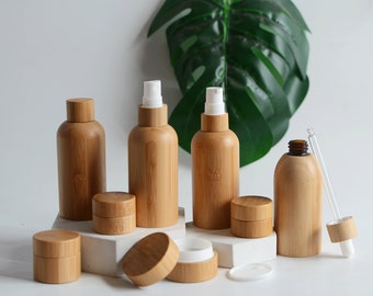 May include: Set of bamboo cosmetic bottles and jars with white pumps and lids. The bottles and jars are arranged on a white surface with a green leaf in the background.