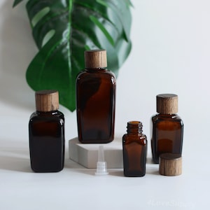 Puede incluir: Cuatro botellas de vidrio ámbar con tapas de madera, una con un gotero de plástico transparente, sobre una superficie blanca. Las botellas son de diferentes tamaños y están dispuestas en fila.