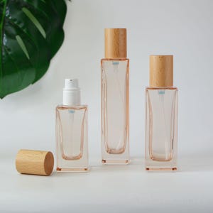 May include: Three glass bottles with wooden caps. The bottles are clear and have a light pink tint. The bottles are different sizes and are arranged in a row from left to right.