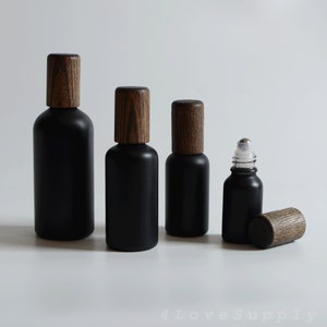 May include: Four black glass bottles with wooden caps. The bottles are different sizes and are arranged in a row from largest to smallest. The bottles are on a white surface.