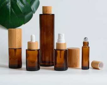 May include: A collection of amber glass bottles with bamboo lids. The set includes a roller bottle, spray bottle, dropper bottle, and a tall cylindrical bottle. The bottles are arranged on a white surface.