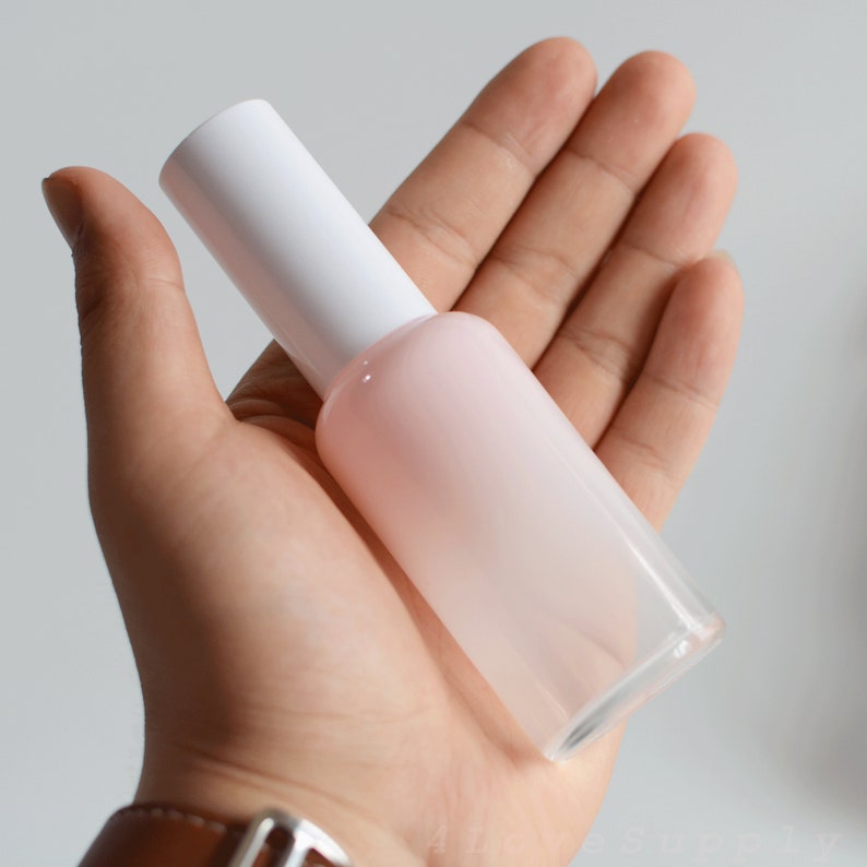 May include: A white and pink frosted glass bottle with a white pump top. The bottle is held in a person's hand.