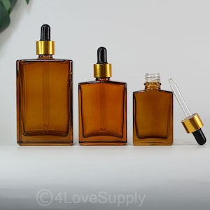 Puede incluir: Tres frascos cuentagotas de vidrio ámbar de diferentes tamaños. Cada frasco tiene forma rectangular con un collar dorado y un cuentagotas negro. Los frascos están dispuestos de mayor a menor.