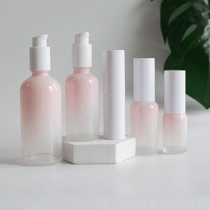 May include: Set of five pink and white glass bottles with pump tops. The bottles are ombre, with a darker pink at the top and fading to white at the bottom.