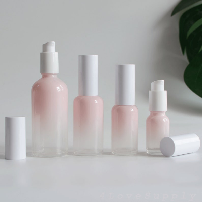 May include: Five glass bottles with white tops and a pink to clear gradient. The bottles are arranged in a row from largest to smallest.