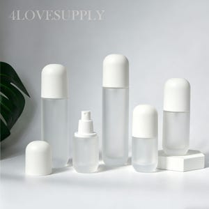 Könnte beinhalten: Eine Sammlung klarer, mattierter Glasflaschen und -behälter mit weißen Deckeln und einem Sprühkopf. Die Flaschen variieren in Größe und Form, mit dem Text "4LOVESUPPLY" oben links. Die Behälter sind auf einer weißen Oberfläche angeordnet.