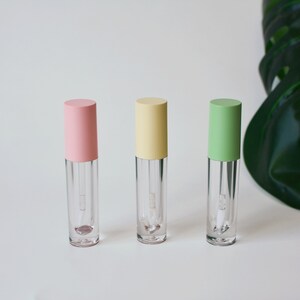 May include: Three clear lip gloss tubes with different colored caps. The caps are pink, yellow, and green.