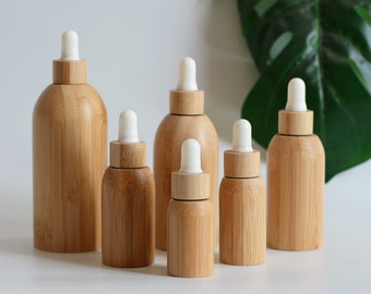 May include: Set of six bamboo essential oil bottles with dropper lids. The bottles are various sizes and are arranged in a row on a white surface.