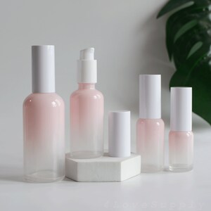 May include: Five glass bottles with white caps and a pink to white gradient. The bottles are arranged in a row on a white surface.