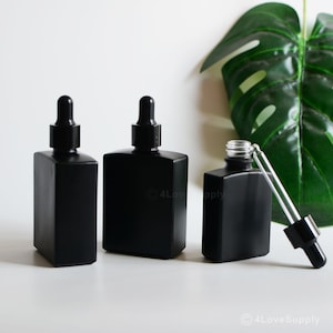 May include: Three black glass dropper bottles with black caps and clear glass droppers. The bottles are square shaped and have a frosted finish. The bottles are on a white surface.