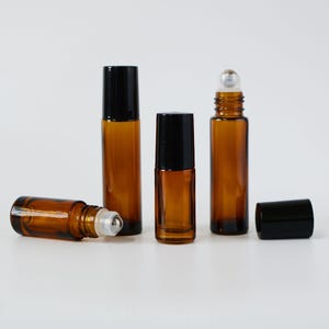 Może przedstawiać: Cztery bursztynowe szklane butelki z rolką z czarnymi nakrętkami. Butelki są puste i gotowe do napełnienia olejkami eterycznymi lub innymi płynami.