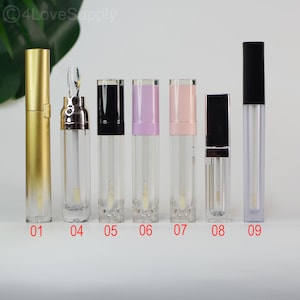 May include: A collection of empty lip gloss tubes with various colored caps, including gold, black, pink, and lavender. The tubes are clear, showcasing the applicator wands inside. The image is taken on a white background.